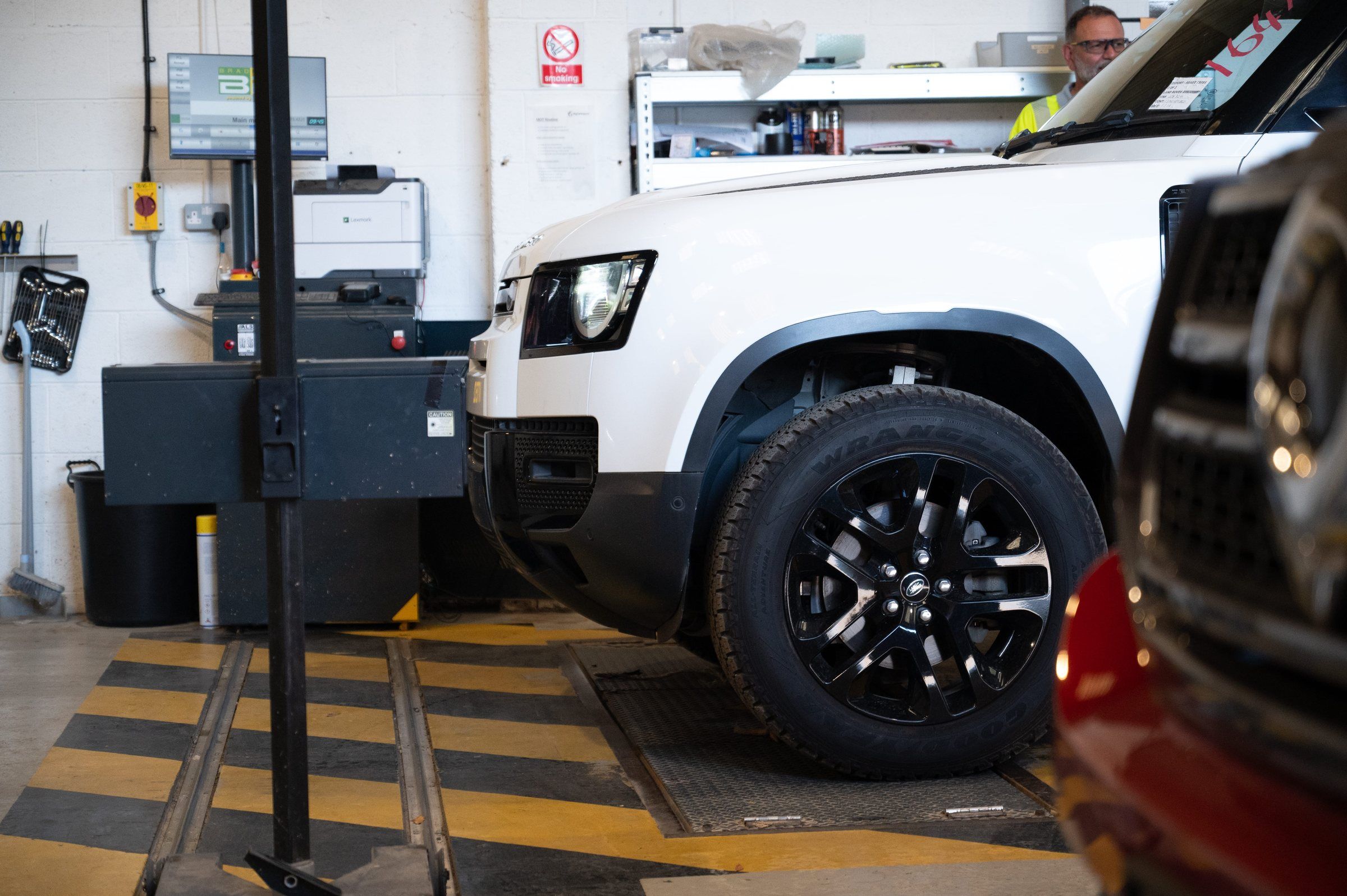 A white Land Rover Defender on the inspection lane in the My Car Import workshop, with a staff member at the test console