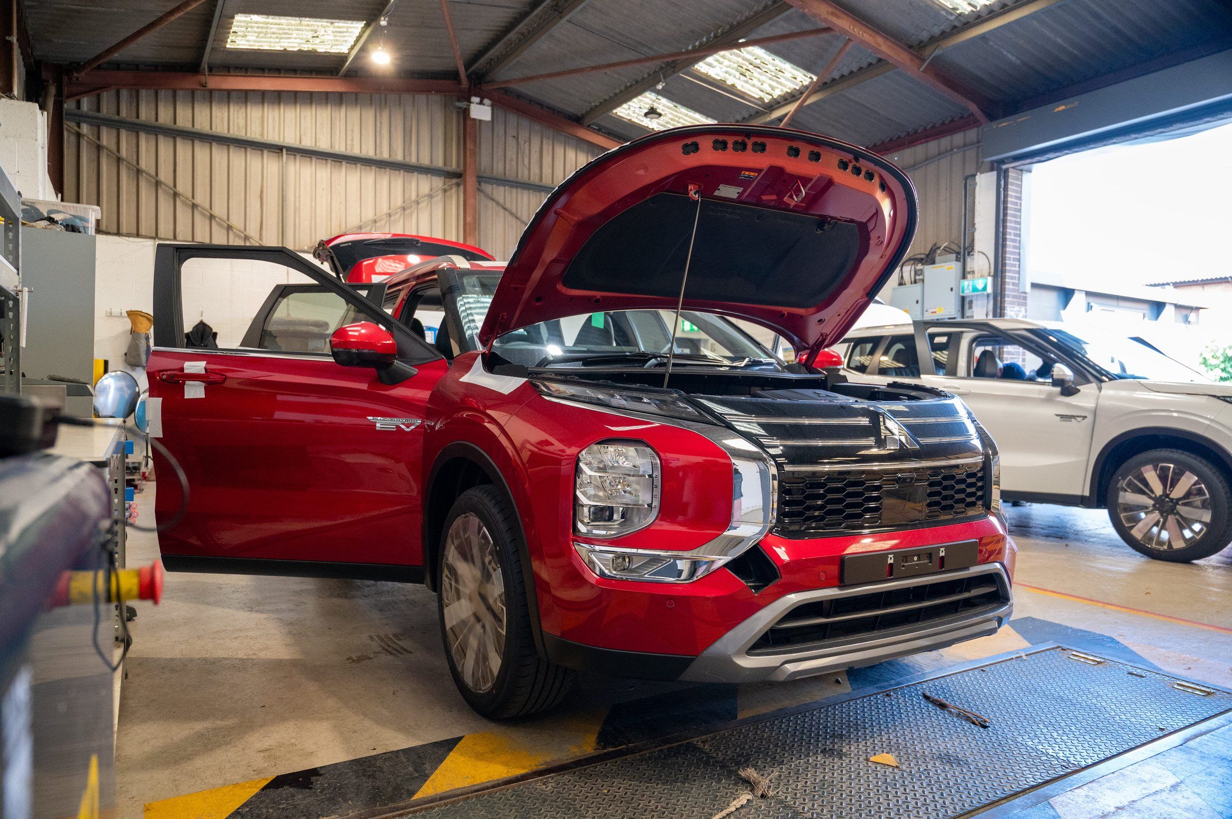 A red Mitsubishi Outlander plug-in hybrid with its doors and bonnet open for inspection in the My Car Import workshop