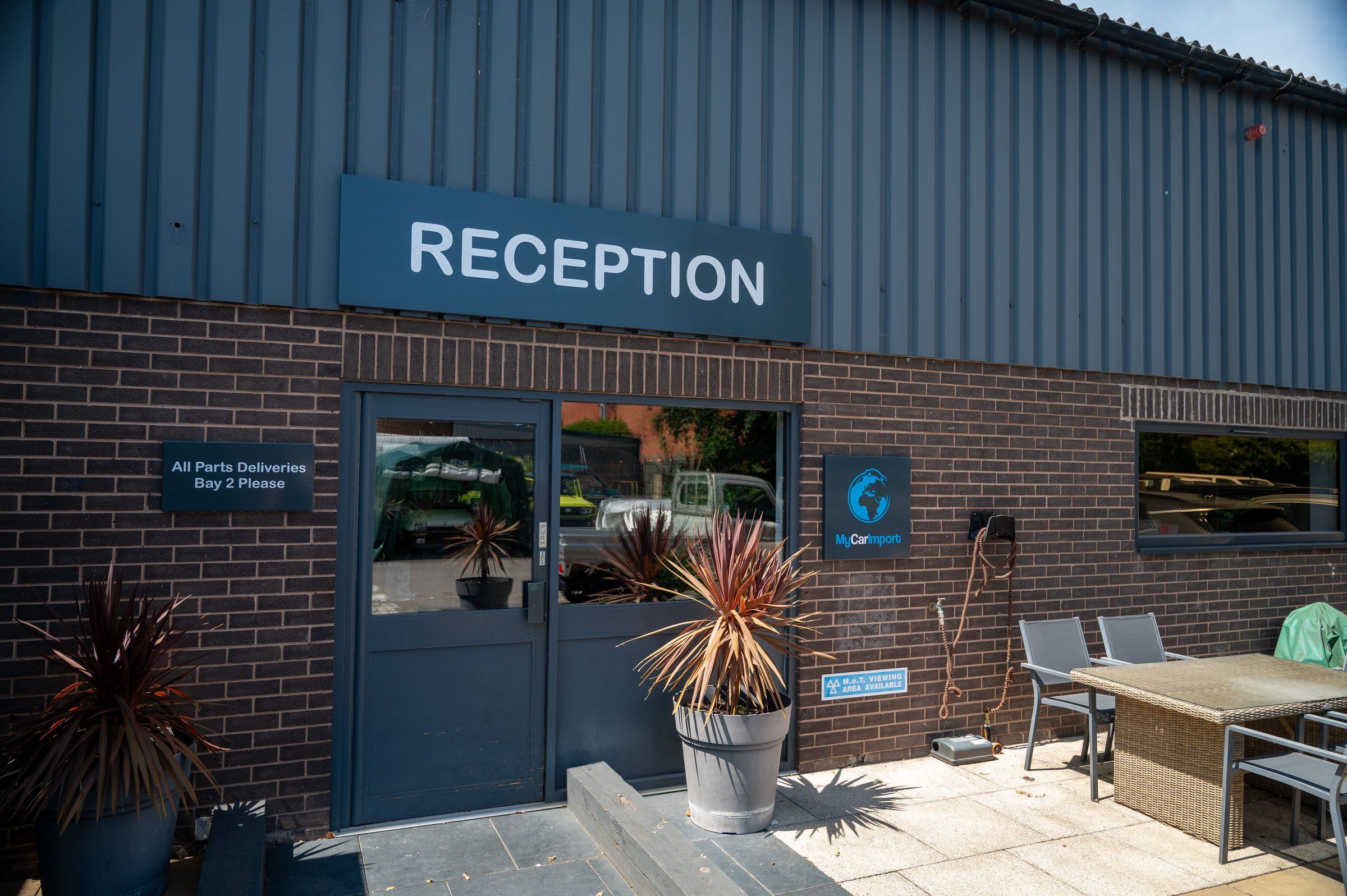 The reception entrance at My Car Import, a brick and blue-clad unit with planters and outdoor seating